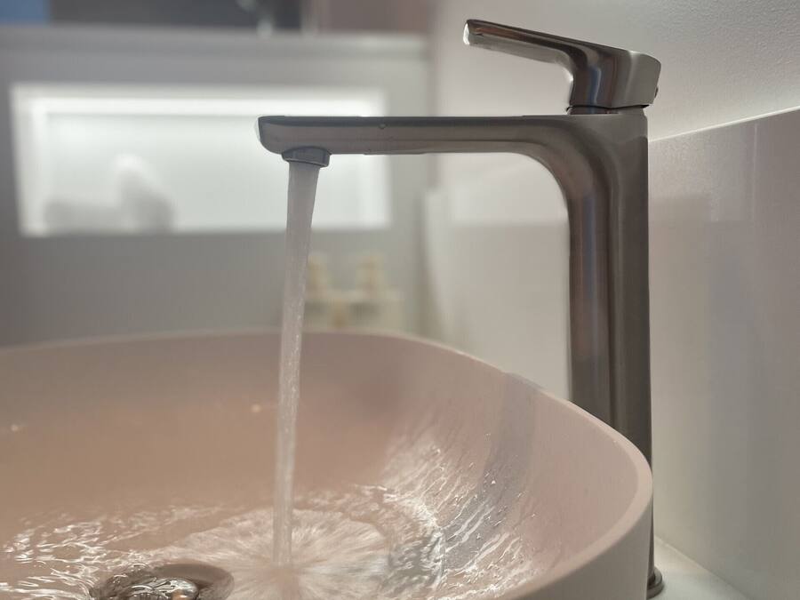 Un lavabo de bany amb aigua corrent, un aireix modern i un mirall a sobre.