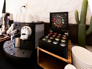 Una cafetera, una exposición de granos de café y un cactus en una habitación.