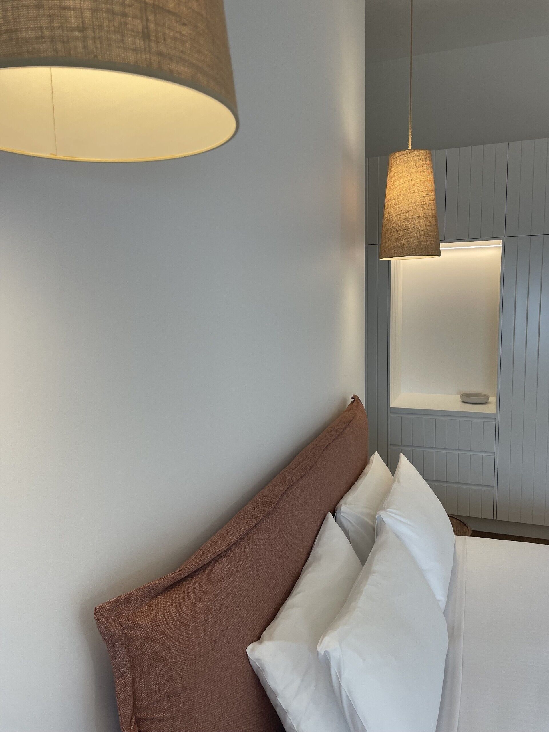 A hotel room with a bed, a hanging lamp, and a wall-mounted light fixture.