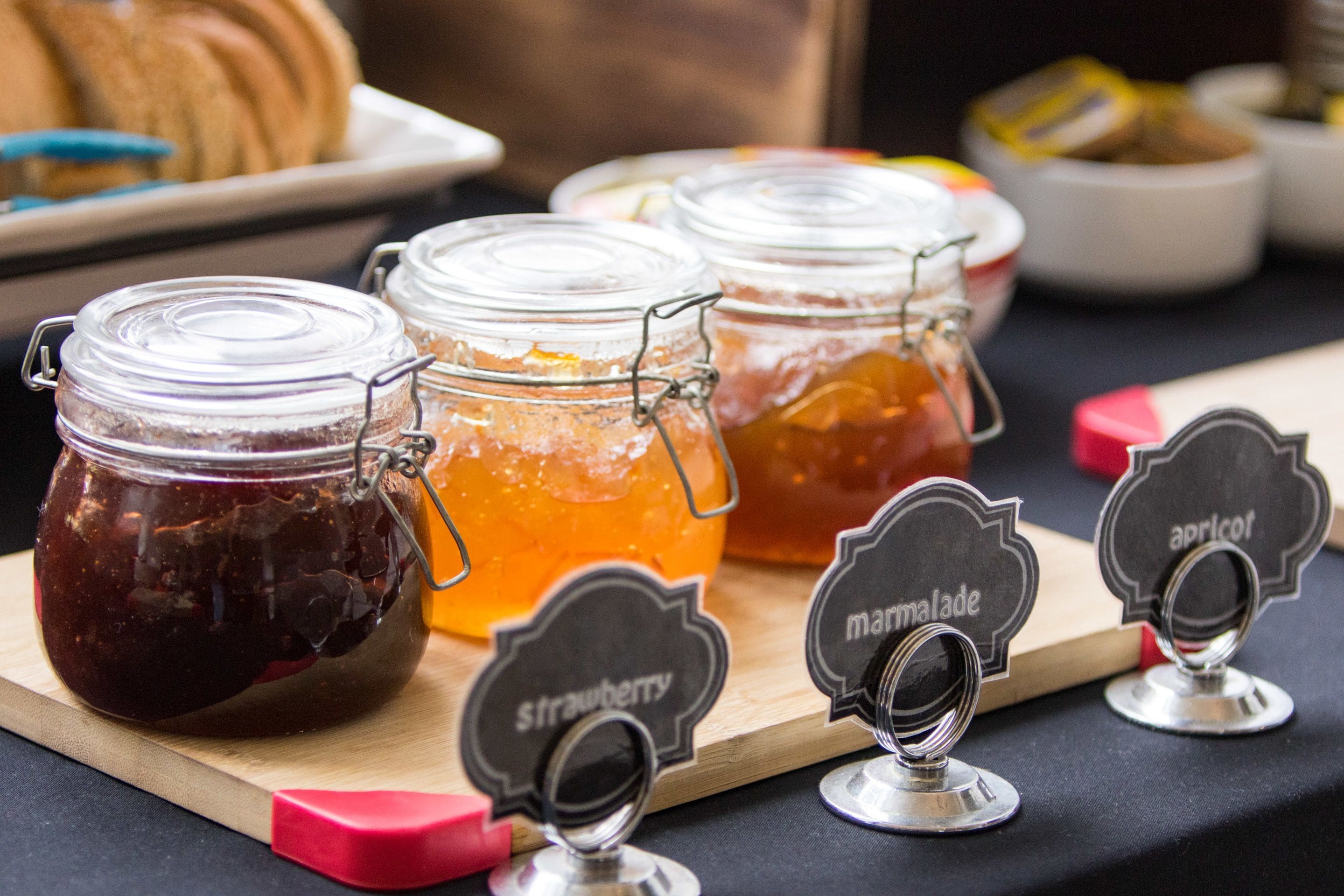 Trois pots en verre avec des couvercles en métal, chacun portant une étiquette indiquant un type de confiture différent.