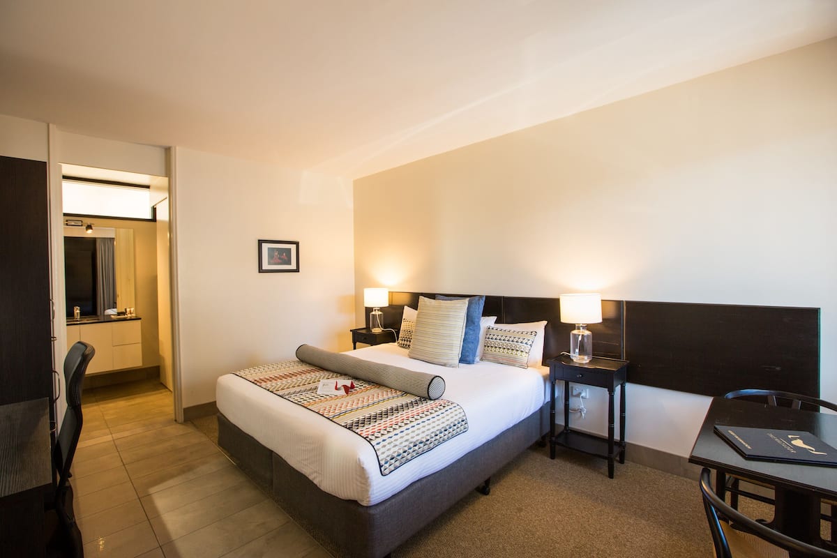 Una habitación de hotel con cama, mesitas de noche, un escritorio y una silla.