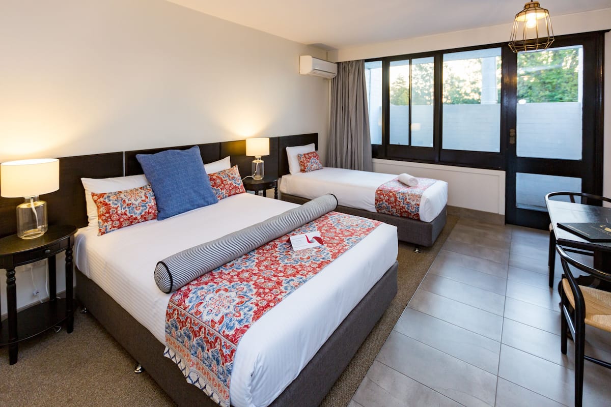 Habitación de hotel con dos camas, una mesa de comedor y vistas al exterior a través de amplias ventanas.