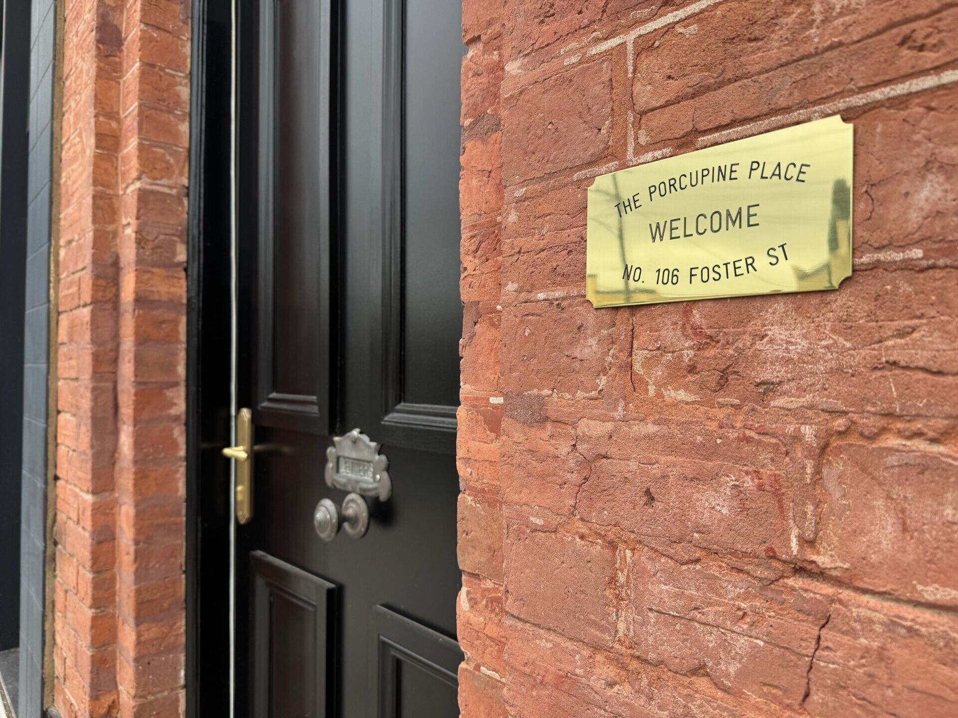 Un muro de ladrillo con un letrero amarillo que dice 'THE PORCUPINE PLACE WELCOME NO. 106 FOSTER ST.'