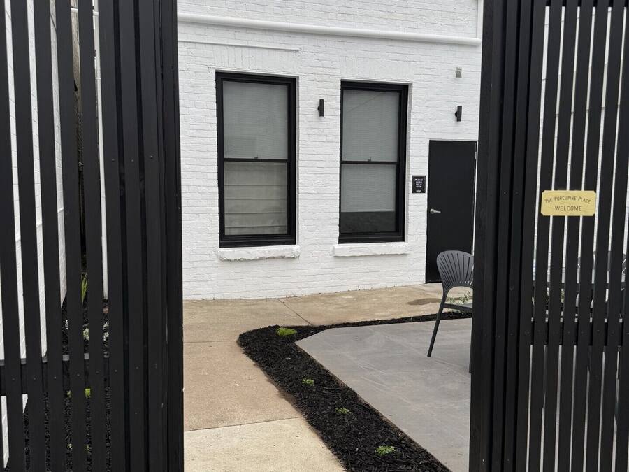 A white building with two windows, a black gate, and a sign that says 'The Porcupine Place Welcome.'