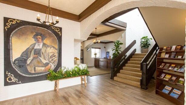 A spacious lobby with a wooden floor, a staircase, a bookshelf, and a large portrait on the wall. - The Matador (Sale)