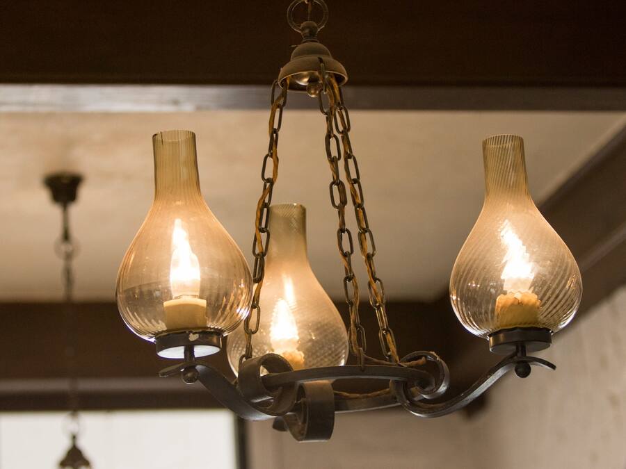A chandelier with three glass shades and a candle.