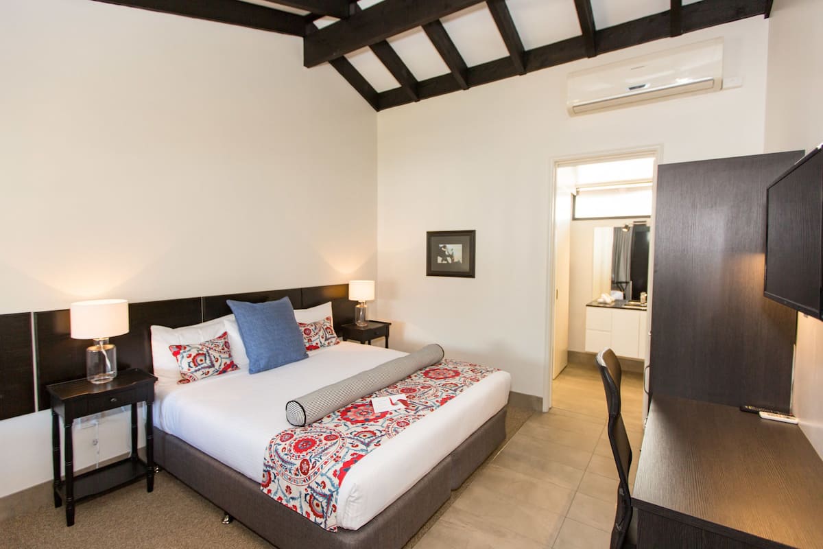 Una habitación de hotel con una cama, dos mesitas de noche con lámparas, un escritorio y una silla.
