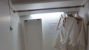 Une petite pièce, de taille modeste, comprenant un lit, une robe suspendue, des chaussons et une petite étagère.