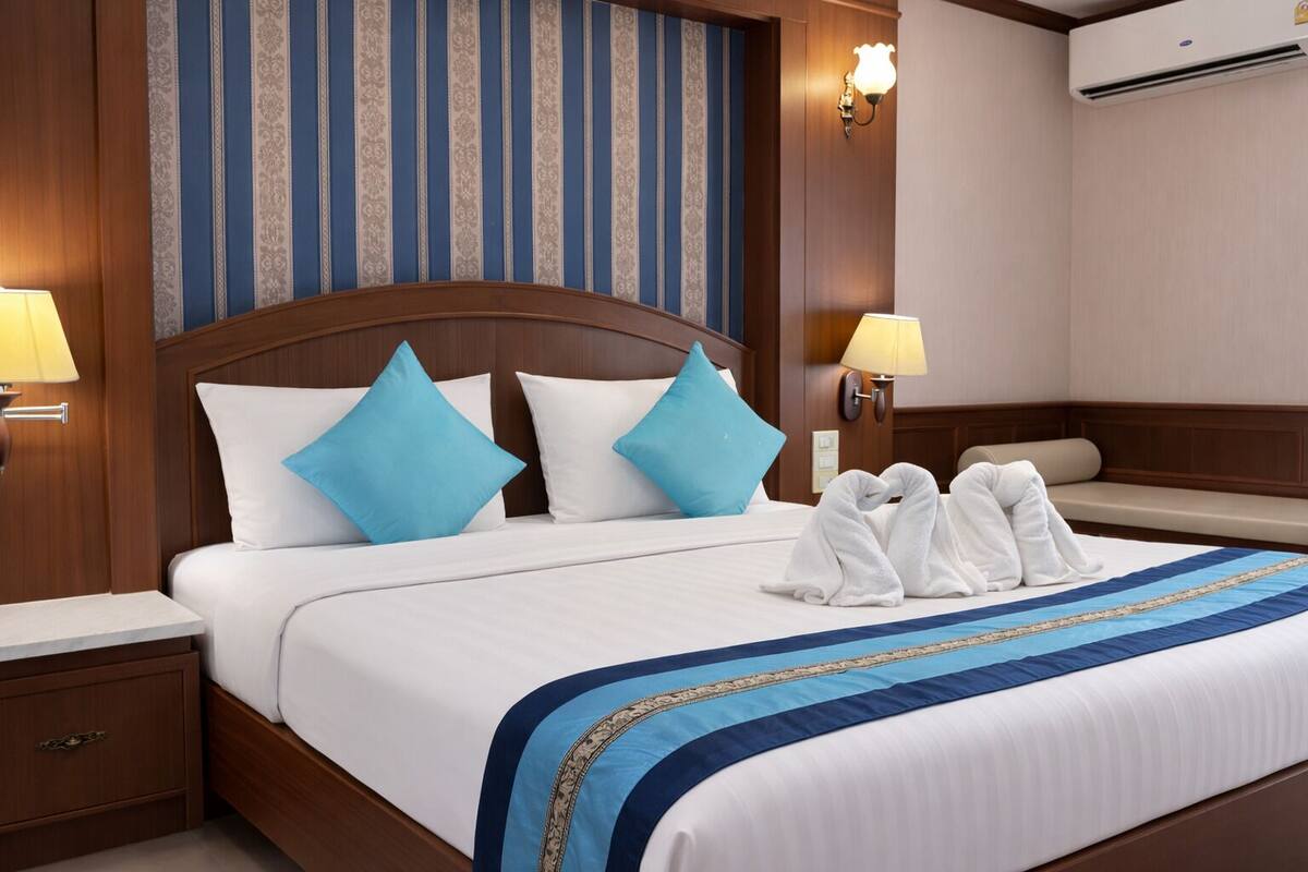 A hotel room with a large bed, two bedside lamps, a wooden headboard, and a wall with vertical stripes.