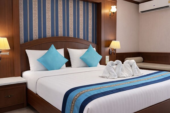 A hotel room with a large bed, two bedside lamps, a wooden headboard, and a wall with vertical stripes. - The Lion King Hotel (Udon Thani)