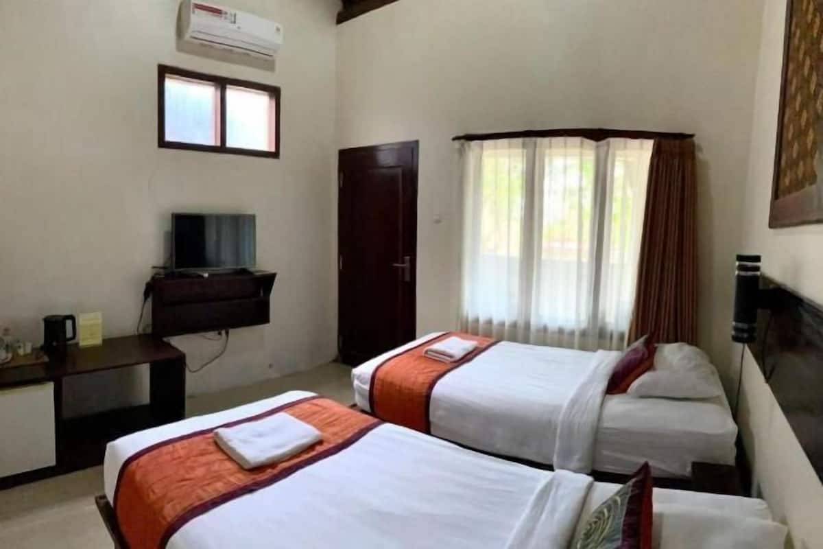 A hotel room with two beds, a desk with a TV, a wardrobe, and a window with curtains.