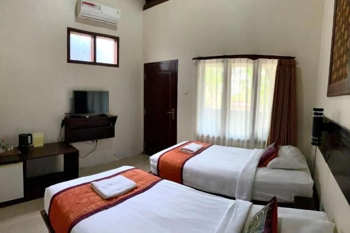 Habitación de hotel con dos camas, un escritorio con televisor, un armario y una ventana con cortinas.