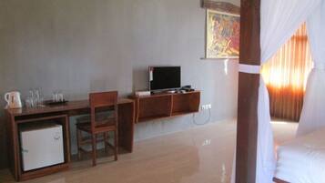 A room with a wooden desk, a television, a small refrigerator, and a bed with white curtains.