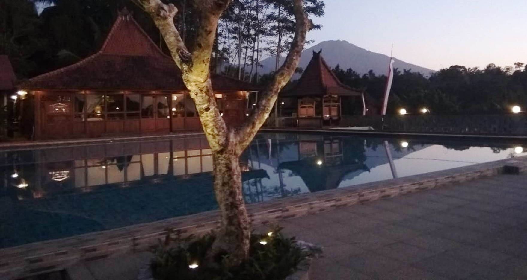 A poolside area with a reflection of a building and a mountain in the background.