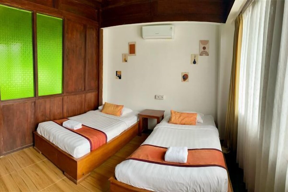 Habitación de hotel con dos camas individuales, paneles de madera, una mesita de noche y aire acondicionado instalado en la pared.