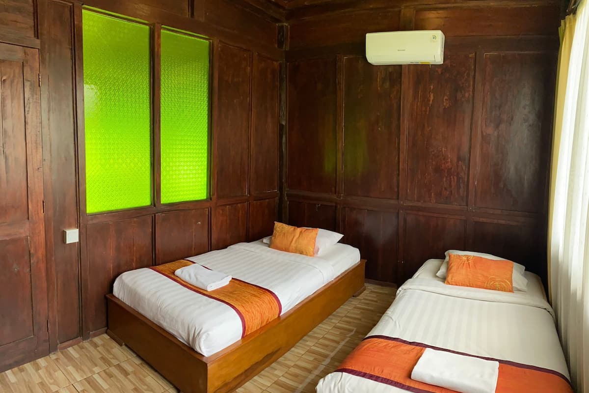 A room with two beds, wooden walls, a green window, and an air conditioning unit.