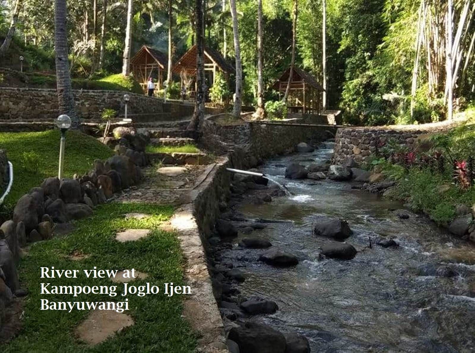 Vista para o rio em Kampoeng Joglo Ijen Banyuwangi, com paredes de pedra e estruturas de madeira.