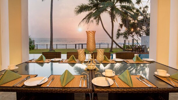 A dining table set for four with a view of the ocean and palm trees. - Villa 46 (Hikkaduwa)