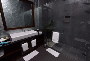 Un bagno moderno con uno specchio grande, piastrelle scure, un lavandino bianco e una zona doccia.