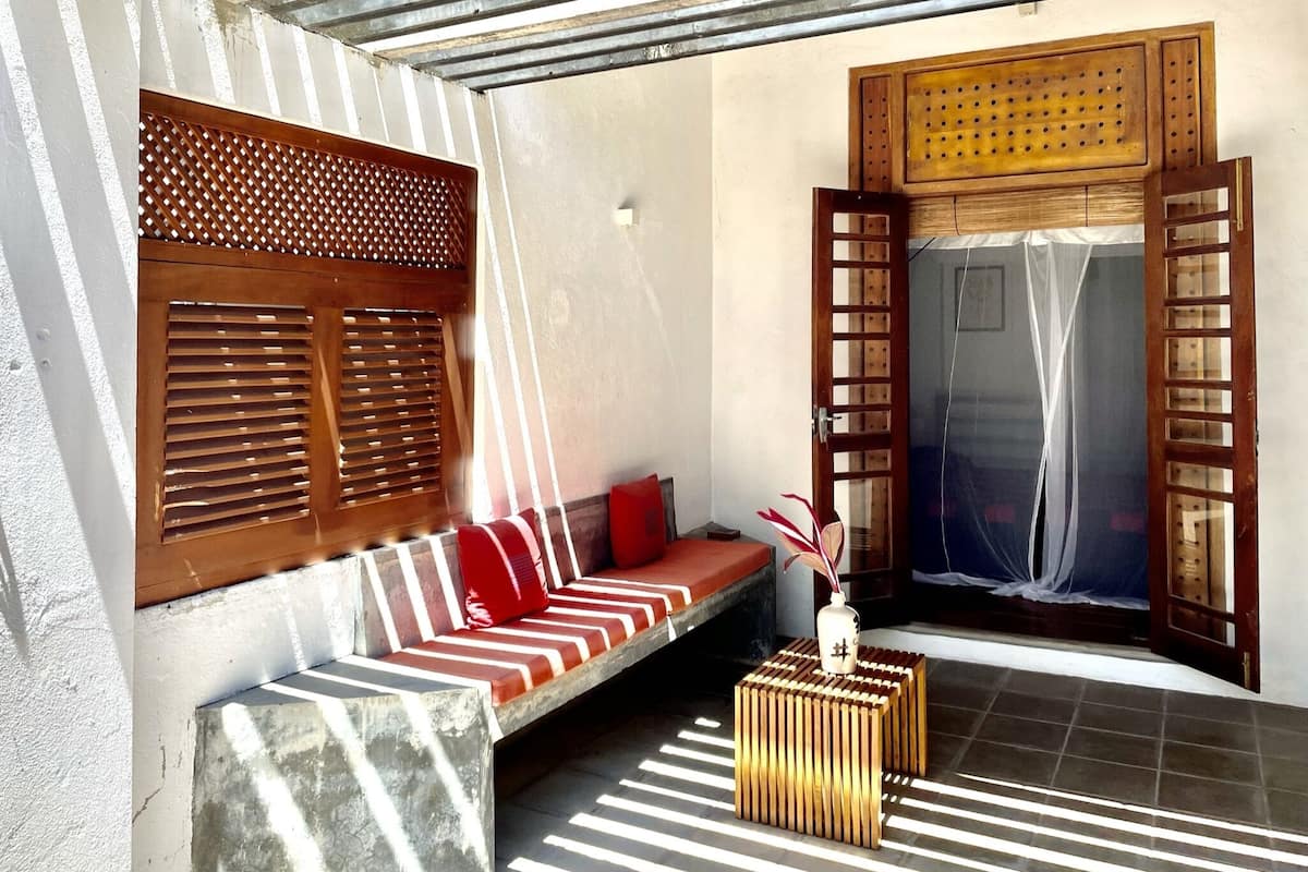 A room with a wooden bench, a small table, and a window with wooden shutters.