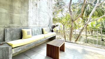 A modern outdoor seating area with a concrete bench and a wooden table, overlooking a garden with palm trees.