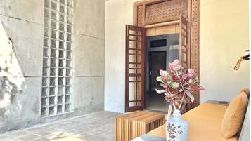 A room with a tiled floor, a wooden bench, a sofa with cushions, a decorative vase, and a wooden door with a lattice design.