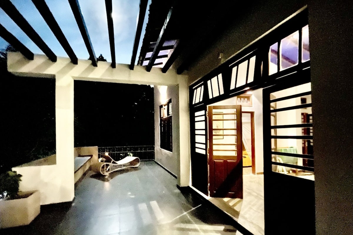 A covered outdoor area with a scooter, a door leading to a room, and a window with blinds.