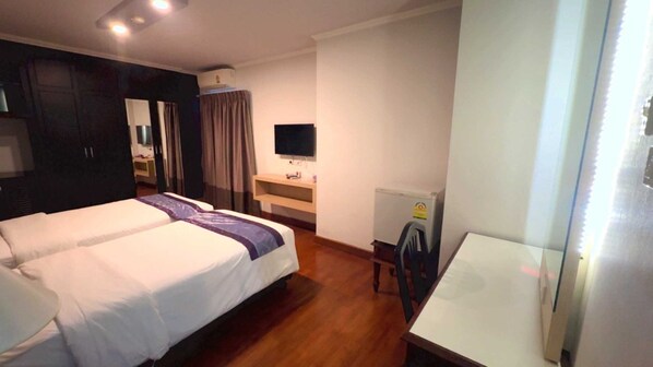 A hotel room with two beds, a desk, a TV, and a radiator.