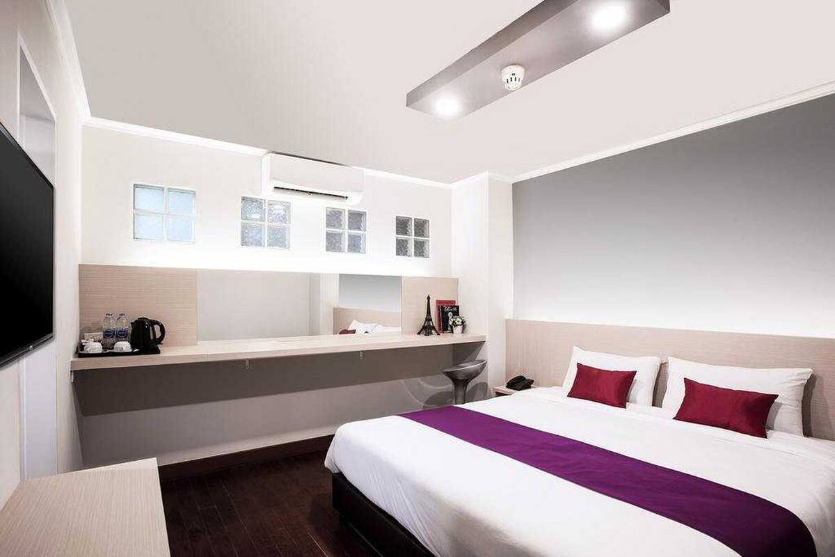 A modern hotel room with a large bed, a flat-screen TV, a desk, and a built-in bench.