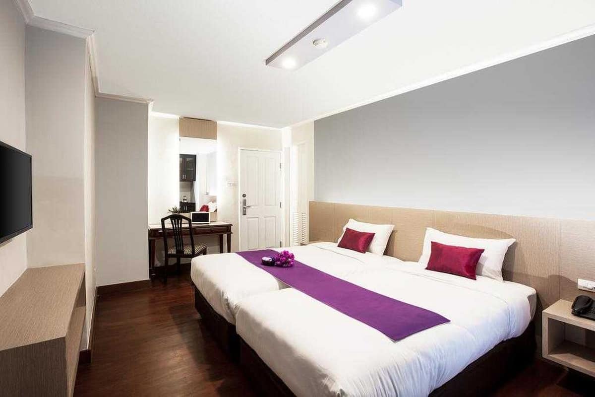 A hotel room with a large bed, a desk, a chair, a TV, and a bedside table.