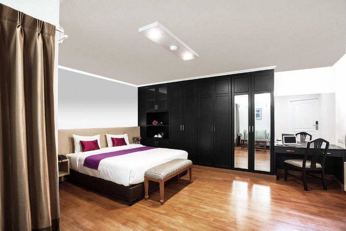 A modern bedroom with a large bed, a desk, and a sliding door leading to a balcony.