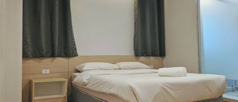 A modern bedroom with a wooden headboard, a small bedside table, a large bed with white bedding, and dark curtains.