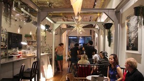 Ένα εστιατόριο με ρουστίκ διακόσμηση, εμφανείς σωλήνες στην οροφή, κρεματά φυτά και ένα κεντρικό φωτιστικό σε σχήμα αστεριού.