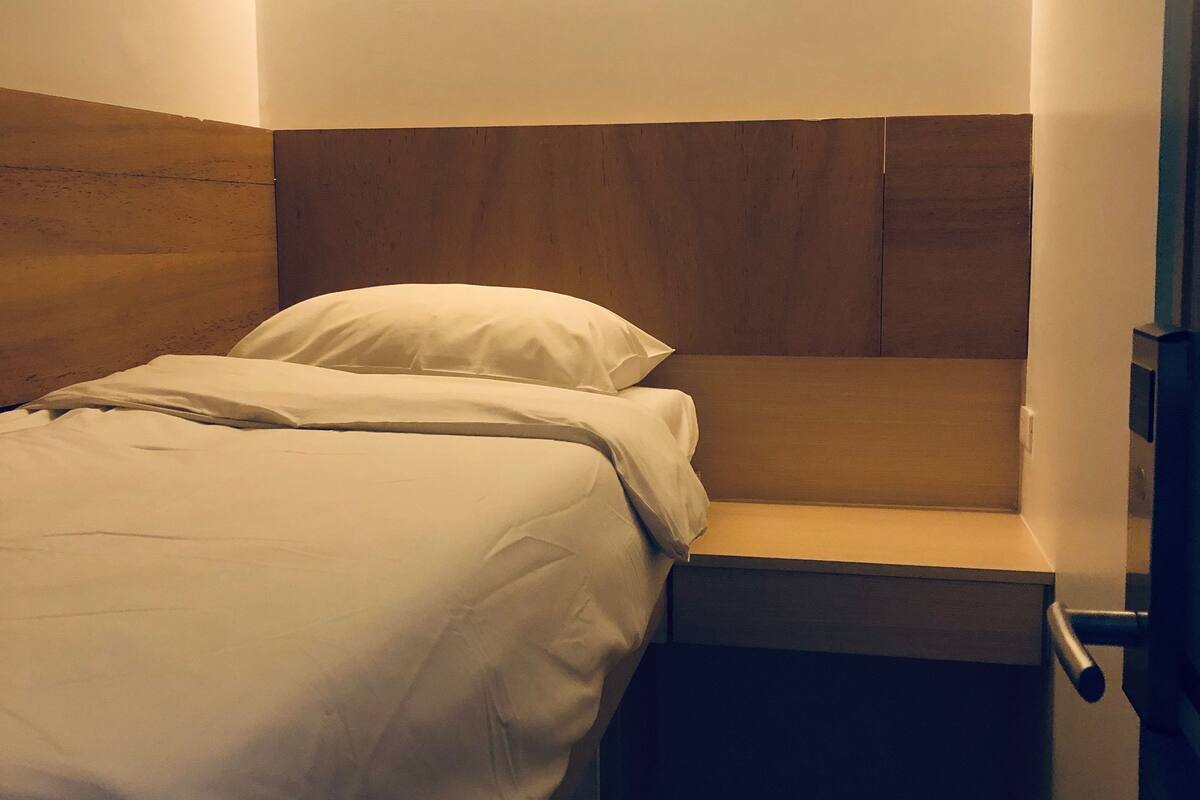 A small, single-bed room with a wooden headboard and a bedside table.