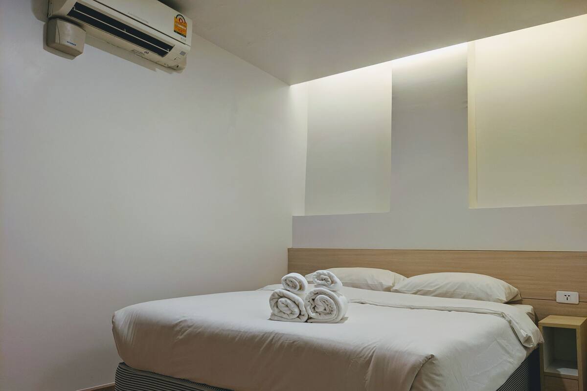 A hotel room with a bed, a wall-mounted air conditioner, and a bedside table.