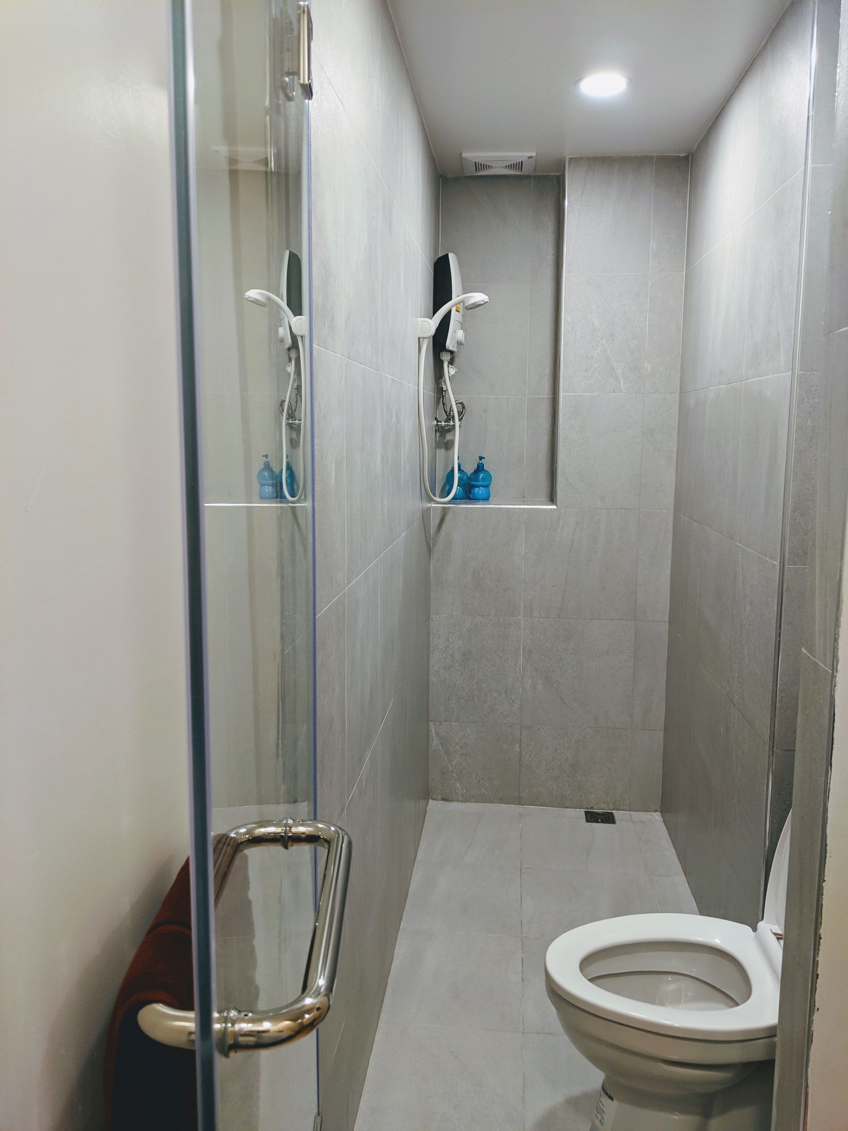 A compact bathroom with a glass shower enclosure, a toilet, and a small shelf with toiletries.
