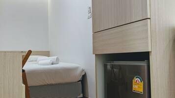 Ein kleines Zimmer mit Bett, Schreibtisch, Kühlschrank und Klimaanlage.