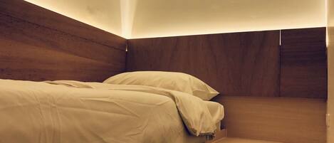 Una cama pequeña y ordenada con cabecera de madera y mesita de noche.