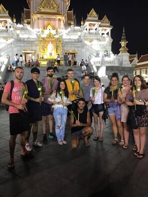 A group of people posing in front of a grand, illuminated temple with multiple tiers and golden decorations. - Good One Poshtel & Café Bar (Bangkok)