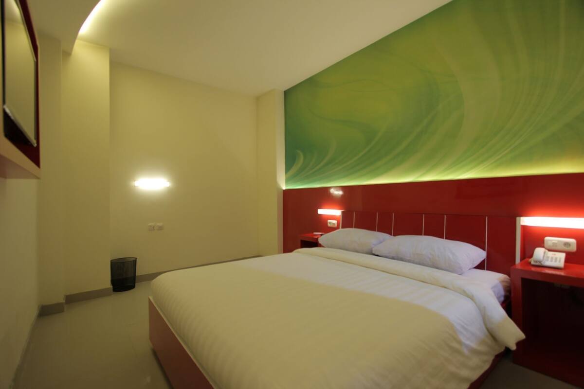 Quarto de hotel com cama, mesas de cabeceira e uma parede com desenho abstrato em tons de verde.