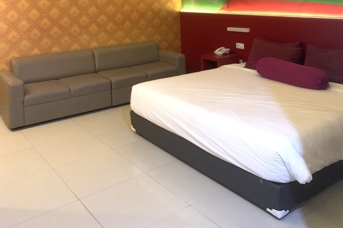 Quarto de hotel moderno com cama, sofá cinza e parede estampada.