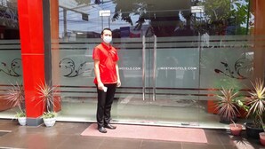 A person standing in front of a hotel entrance with glass doors, potted plants, and a red pillar. - Liberta Hub Singosari Malang (Malang)