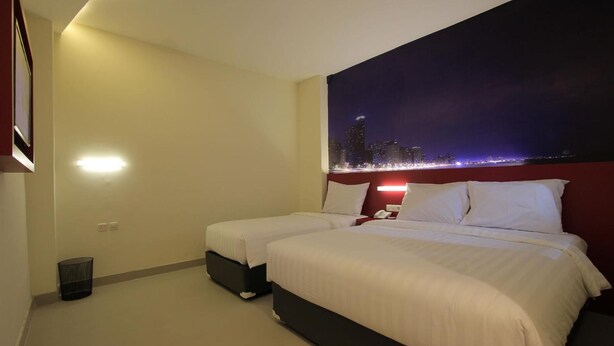 A hotel room with two beds, a cityscape view, and a red accent wall. - Liberta Hub Singosari Malang (Malang)