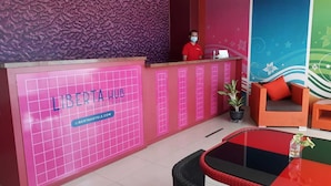 A reception area with a pink grid pattern, a receptionist, and a seating area with a sofa and chairs. - Liberta Hub Singosari Malang (Malang)