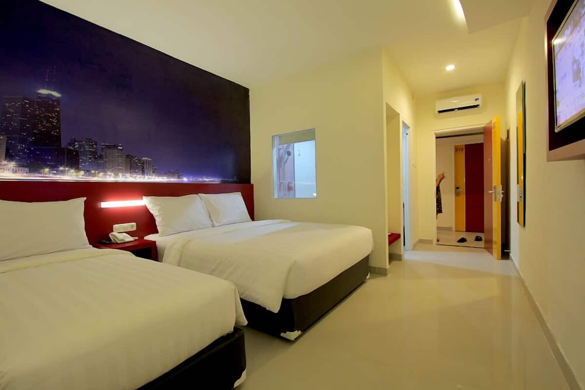 Quarto de hotel com duas camas, vista para a cidade, parede de destaque vermelha e corredor que leva a uma porta com o número 212.