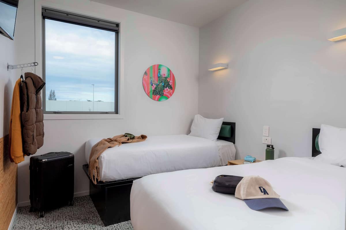 Habitación de hotel con dos camas, una ventana con vistas, un perchero y una maleta.