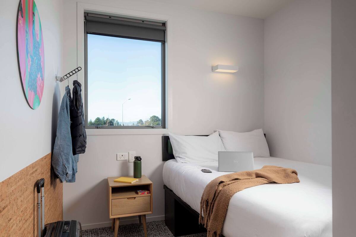 Una habitación de hotel moderna con cama, laptop, maleta y ventana con vistas.