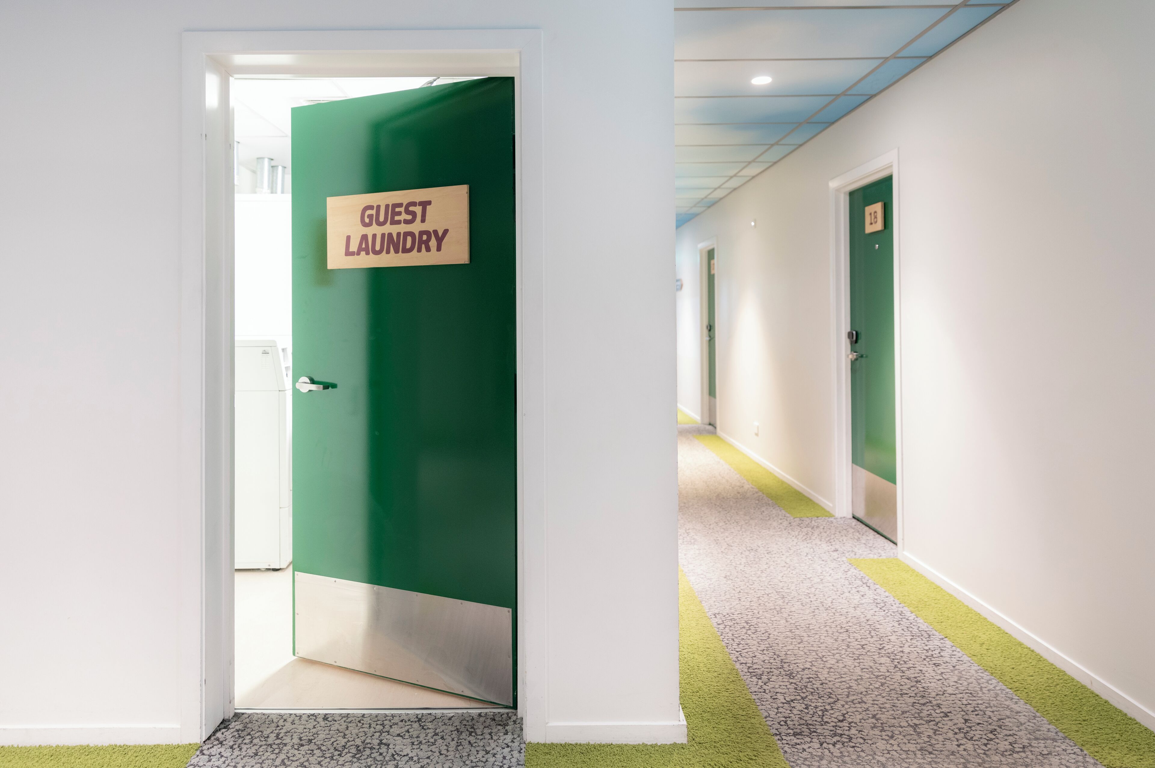 Een hal met een groene deur waarop 'Logieswasserij' staat en een vloerkleed.