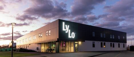 Un edificio moderno con un llamativo letrero 'LyLo', un estacionamiento y una farola.