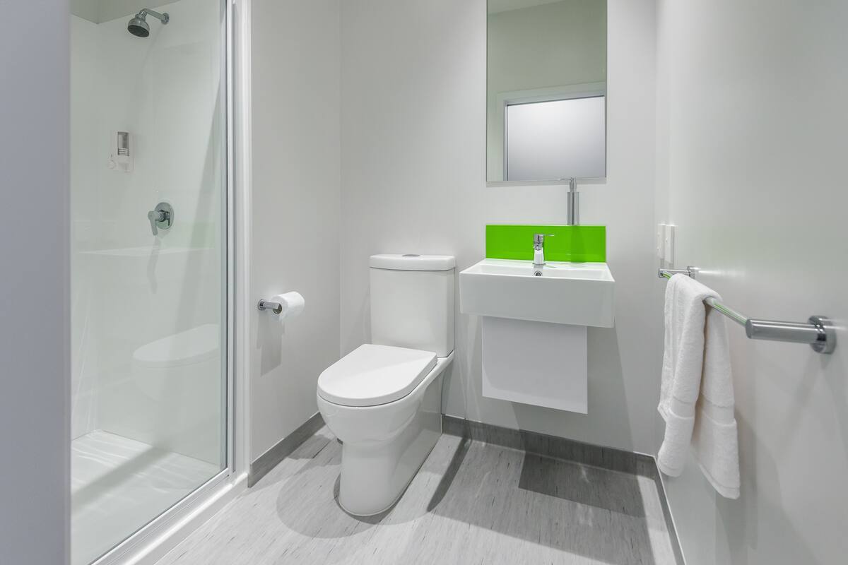 Un baño moderno con cabina de ducha de vidrio, inodoro blanco y lavamanos de tono verdoso.
